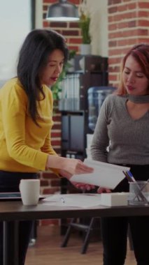 Dikey video: Ofis çalışanları yeni fikirler üretmek için dijital tablet ve kağıtları kullanarak proje uygulamasını araştırmak üzere toplanıyorlar. İş yerinde briwfing stratejisi için bilgi taşıyan Asyalı kadınlar.