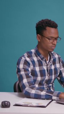 Dikey video: Yorgun çalışan masa başında dinleniyor ve kameranın önünde baş parmağını kaldırıyor, ofis işinde uykulu hissediyor. Yorgun adam iyi ve onay sembolü gösteriyor. Tamam jest