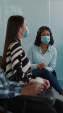 Vertical video: Multiethnic group of applicants receiving employment papers, preparing to start executive job interview with HR department. People waiting in lobby to attend meeting during pandemic.