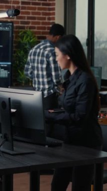 Vertical video Software engineer typing source code on computer keyboard while colleagues sit down at desk for group project. App developer working in it startup company doing online cloud computing.