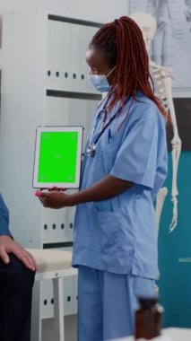 Vertical video: Woman and elderly man with face mask using greenscreen on tablet, isolated display. Nurse and patient looking at chromakey template with mockup background and blank copyspace in