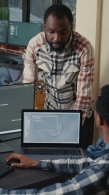 Vertical video Programer sitting at desk with multiple screens running code talking with colleague about artificial intelligence algorithm. Software developers doing innovative artificial intelligence