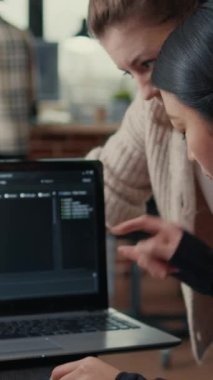 Yazılım geliştiricilerinden oluşan dikey video ekibi masadaki yapay zeka sunucu odasında otururken laptop ekranında çalışan kaynak kodlar hakkında konuşuyor. Veri kodlaması üzerinde işbirliği yapan veritabanı yöneticileri