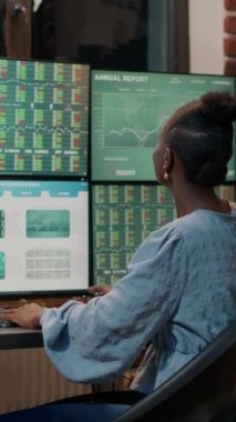 Vertical video: Fund trader working with real time stocks on multi monitors, looking at market exchange statistics and numbers. Trade sales investment graphs to plan new selling strategy. Tripod shot