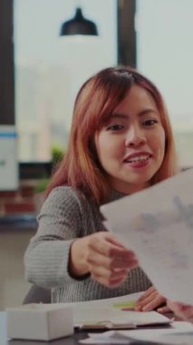 Vertical video: Coworkers doing teamwork to analyze graphics on files in company office. Business people working in collaboration to plan strategy and investment for management career. Partners