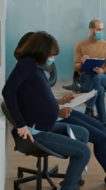 Vertical video: Woman with pregnancy belly dropping cv files on floor while she waits to start job interview appointment. Female candidate helping pregnant person with resume documents in lobby.