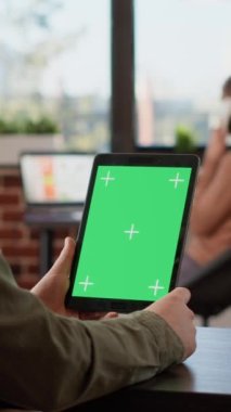 Dikey video: Yeşil ekran ekranlı dijital tablet tutan erkek serbest yazar, boş krom anahtar arka planına bakıyor. Cihaz ekranındaki izole edilmiş telif alanı şablonu analiz ediliyor, şirket bürosu masası.