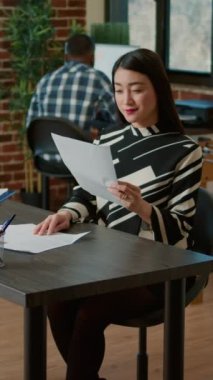 Vertical video: Portrait of asian HR recruiter analyzing cv resume of candidate before job interview meeting. Business woman preparing for work application appointment with recruit in company office.