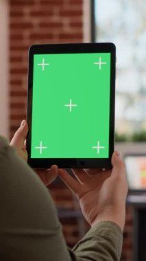 Dikey video: Ofis çalışanı dijital tablet üzerindeki yeşil ekran şablonunu analiz ediyor, cihaz üzerinde izole edilmiş krom anahtarla iş üzerinde çalışıyor. Boş model ve telif alanı arkaplanı ile ekrana bakılıyor.