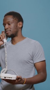 Dikey video: Stüdyoda sabit telefon görüşmesine cevap veren genç adam, ofis telefonunda kablolu yayınla uzaktan konuşma yapıyor. Telgraf kablosu ile iletişim aygıtı üzerinde tartışan kişi