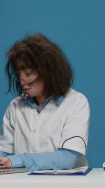 Dikey video: Kamerada dizüstü bilgisayar ve belgeler kullanan çılgın bilim adamı, çılgın yüz ifadeleri yapıyor ve deli gibi davranıyor. Duman patlamasından sonra dağınık saçlı, aptal, komik kadın..