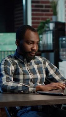 Vertical video: Portrait of african american man using laptop to plan global stock trade, working with forex sales and money exchange for business investment. Capital profit growth, index price.
