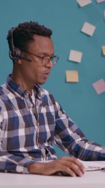 Dikey video: Telepazarlama operatörü müşteri hizmetleri çağrı merkezinde yardım ve destek veriyor, insanlarla telefonda konuşuyor. Satış danışmanı müşteriye mikrofon ve kulaklık kullanıyor.