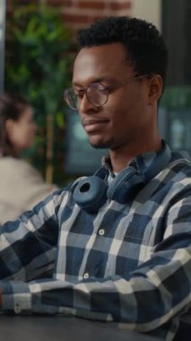 Dikey video portresi, odaklanmış programcının kod düzeltme gözlüğü yazması ve başlangıçta masada oturup gülümsemesi. Arka planda çalışan programcı takımıyla kodlayıcı programlama arayüzü.