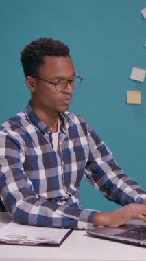 Dikey video: Genç yetişkin yorgun hissediyor ve iş büyümesini planlamak için dizüstü bilgisayar kullanıyor. Yorgun çalışan kendini uykulu ve hayal kırıklığına uğramış hissediyor, masa başında fazla mesai yapıyor..