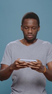 Dikey video: Modern insan akıllı telefonda video oyunları oynuyor, internet ağındaki mobil oyun aktiviteleriyle eğleniyor. Erkek model telefonda siber uzay yarışmasının tadını çıkarıyor.