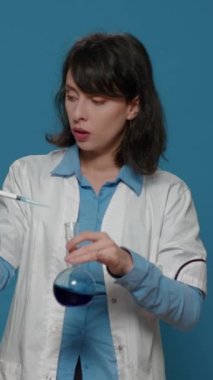Dikey video: Kadın bilim adamı mikro pipeti kullanarak beherin içine sıvı damlatıyor, maddeyle kimyasal deney yapıyor. Laboratuvar ekipmanlarıyla biyokimya geliştirme üzerine çalışan bilim uzmanı