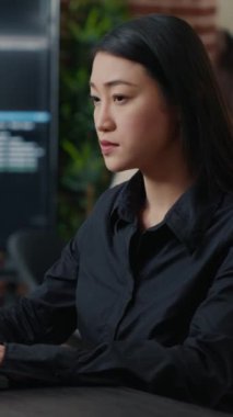 Gülümseyen Asyalı programcının dikey video portresi yazılım geliştirme ofisinde masa başında kod yazmaya odaklandı. Sistem mühendisi başlangıç şirketi için algoritma oluşturmaya odaklanıyor.