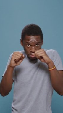 Dikey video: Saldırgan adam yumruklarını sıkıyor ve kamera karşısında eklemlerini kaldırıyor, kızgın hissediyor ve hava yumrukları atıyor. Öfkeli şiddet yanlısı zorba stüdyoda savaşmaya ve protesto etmeye hazırlanıyor.