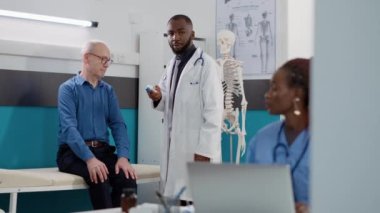 Genel pratisyen hekim eski bir hastanın ateşini ölçmek için termometre kullanıyor. Erkek doktor, üst düzey doktorla sağlık danışmanlığında sıcaklık ölçümü yapıyor..