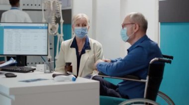 Engelli yaşlı bir adam ve karısı doktorla kabinede tıbbi bir randevusu var. Tekerlekli sandalyedeki hasta salgın sırasında uzman, sağlık desteğine danışmanlık yapıyor..