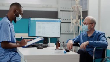 Sağlık çalışanı fiziksel yetersizlikten muzdarip kıdemli bir adamla görüşmede notlar alıyor. Coronavirüs salgını sırasında tekerlekli sandalyedeki erkek kullanıcıya danışmanlık yapmak..