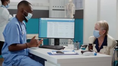 Afrika kökenli Amerikalı hemşire tekerlekli sandalyedeki hastaya danışmanlık yapıyor, kovid 19 salgını sırasında check-up randevusu alıyor. Kronik maluliyeti olan tıbbi asistan ve kadın muayene ediyorlar..
