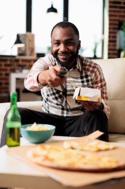Erişte teslimat kutusu tutan ve uzaktan kumandayla film arayan genç bir adam. Yemek çubuklarıyla fast food yemek, televizyonda film izlemek, eğlenmek..