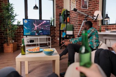 Modern male person playing video games on tv console, using strategy to play action shooting game with group of friends and gathering with alcoholic drinks. People having fun.