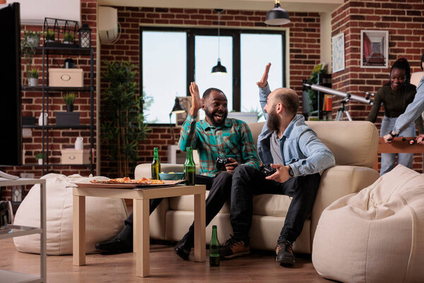 Multiethnic team of people doing highfive gesture after winning video games play on television console. Celebrating competition victory together at house party and gathering with friends.