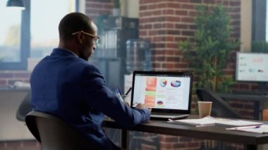 Şirket çalışanı, online sunum yapmak için bilgisayardaki iş bilgilerini analiz ediyor. İdari araştırma istatistiklerini kullanan ofis çalışanı, web sitesi uygulamasında başlangıç projesi planlıyor.
