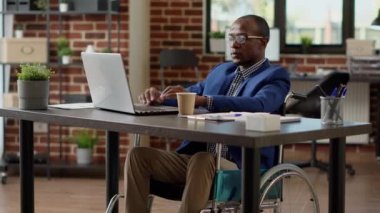 Fiziksel kronik engelli bir iş adamı dizüstü bilgisayarda çalışıyor, ağ kullanıyor. Felç olmuş tekerlekli sandalye kullanıcısı, maluliyet dostu ofiste acı veren sağlık sorunları yaşıyor..