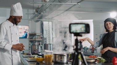 Çok ırklı aşçılardan oluşan bir ekip çevrimiçi yemek programı sunuyor, restoran mutfağında kamera önünde video çekiyor. Erkek ve kadın gastronomik aşçılık kursu yapıyor, yemek tarifi hazırlıklarını kaydediyor..
