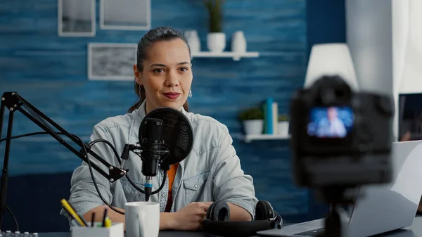 Popular social media influencer sitting at home studio desk while recording vlog. Creative internet content creator hosting show in living room while having modern audio equipment.