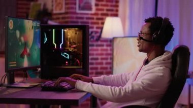 Oyuncu evde rahatlamak için bilgisayar oyunu kurulumu kullanarak hızlı tempolu çoklu oyuncu uzay nişancısı yarışması yapıyor. Afrika kökenli Amerikalı adam kulaklık kullanarak konuşurken online simülasyon oyunu oynuyor.