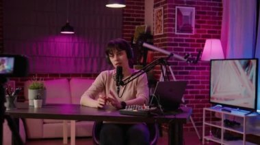 Ev podcast stüdyosunda dijital video kamera ile video bloğu kaydederken internet radyo yayını yapan bir kadının portresi. İçerik yayınlanırken kulaklıklı talk show sunucusu gülümsüyor.