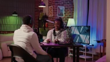 African american online radio host talking in interview with influencer for entertainment internet show late at night in home studio. Portrait of woman recording podcast with male singer celebrity.