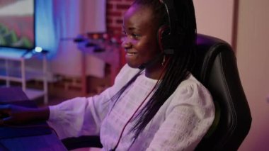 Bilgisayarda oynarken mikrofona mikrofon takan Afro-Amerikan bir kadının aşırı yakın çekimi. Oyuncu kız online yarışmada takıma aksiyon oyunu taktiklerini açıklıyor.