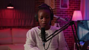 Portrait of african american woman influencer reading content from laptop sitting at desk in home recording studio. Online radio host smiling confident at camera while broadcasting live.