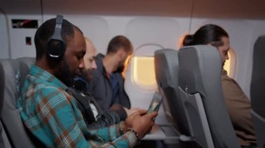 Günbatımında uçak uçuşunda akıllı telefon kullanan erkek turist, tatil yerine zaman geçirmek için internete göz atıyor. Ekonomi sınıfında uçmak ve telefon kullanmak. El kamerasıyla..