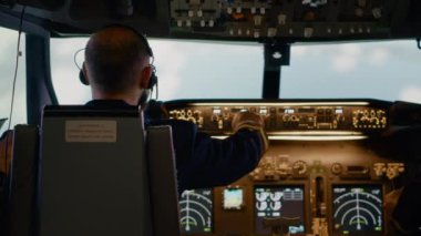 Erkek havayolu kaptanı yükseklik ve boylam düğmelerini tamir ediyor, kontrol paneli ve kontrol panelini kullanıyor. Hava mürettebatı ve radar pusulası, güç motoru ve ön camı olan bir uçak..