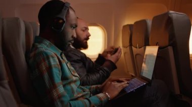 Uçuşta dizüstü bilgisayar kullanan, ekonomi sınıfında gün batımında iş seyahatinde olan Afrikalı Amerikalı serbest çalışan. Bilgisayarda çalışmak ve uçakla uçmak, havacılık yolculuğu. El kamerasıyla..