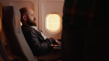 Erkek yolcu seyahat için uçakta yer buluyor, ticari havayolu ile seyahat ediyor. Gün batımında uçakla uçmak, oturmak ve havaalanının inmesini beklemek. El kamerasıyla..