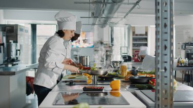 Mutfak sobasında organik sebzeleri kızartan profesyonel bir aşçı. Mutfak tarifi için yemek hazırlıyor. Üniformalı kadın gastronomik mutfak yemeği ve içinde malzemeler olan gurme tabağı pişiriyor..