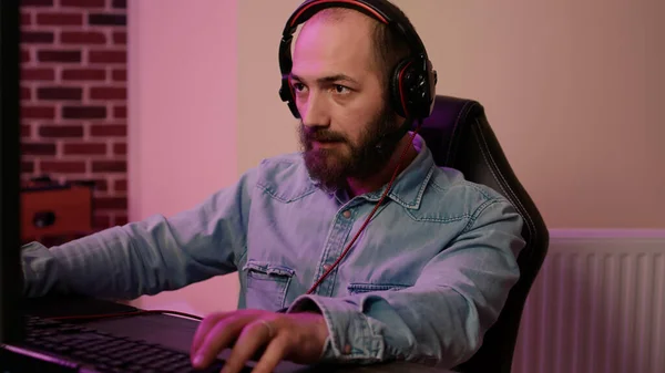 Closeup of man with gaming headset playing multiplayer online action game streaming gameplay on professional pc setup. Gamer looking at computer screen while talking to team members in tournament.