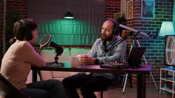 Online radio station host interviewing guest in late night talk show recording podcast using professional microphone and audio mixer. Man having casual converastion with woman in internet broadcast.