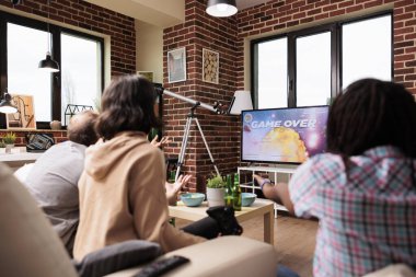 Modern konsolda oyun raundunu kaybederken ekranda oyuna tepki veren üzgün bir kadın. Sıradan oyuncular, yakın arkadaş grubuyla oturma odasında kanepede otururken maç kaybettiği için kızgınlar..