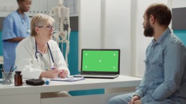 Physician and patient analyzing greenscreen template on laptop, using technology in cabinet. Medic explaining chromakey background with isolated copy space and blank mockup. Tripod shot.