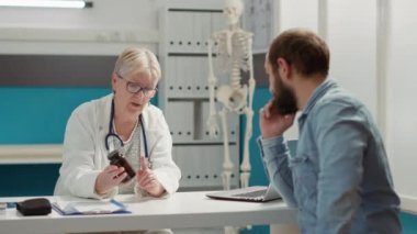 Kadın doktor, reçeteli ilaçları şişede açıklıyor, genç hastaya sağlık kontrolünde hap, ilaç ve ilaç veriyor. Vitamin ve ağrı kesicilerle ilaç tedavisi.