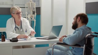 Health specialist doing consultation with paralyzed patient in disability friendly office. Wheelchair user suffering from physical health condition and impairment, receiving disability advice.